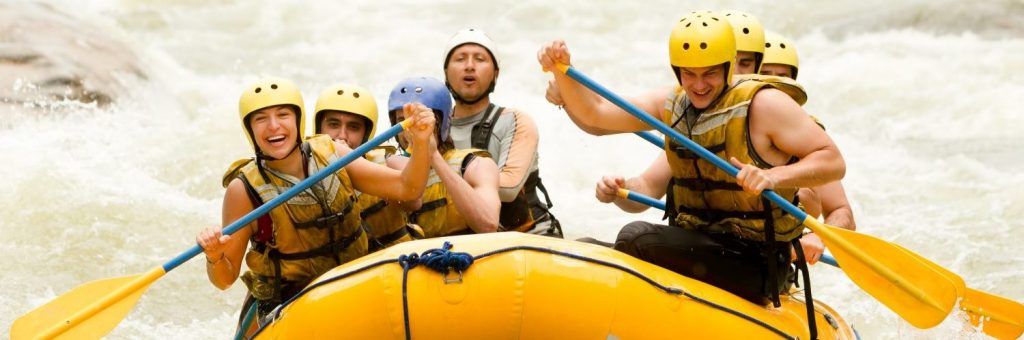 Individuals in lifejackets and helmets white water rafting in a tube with water splashing around them