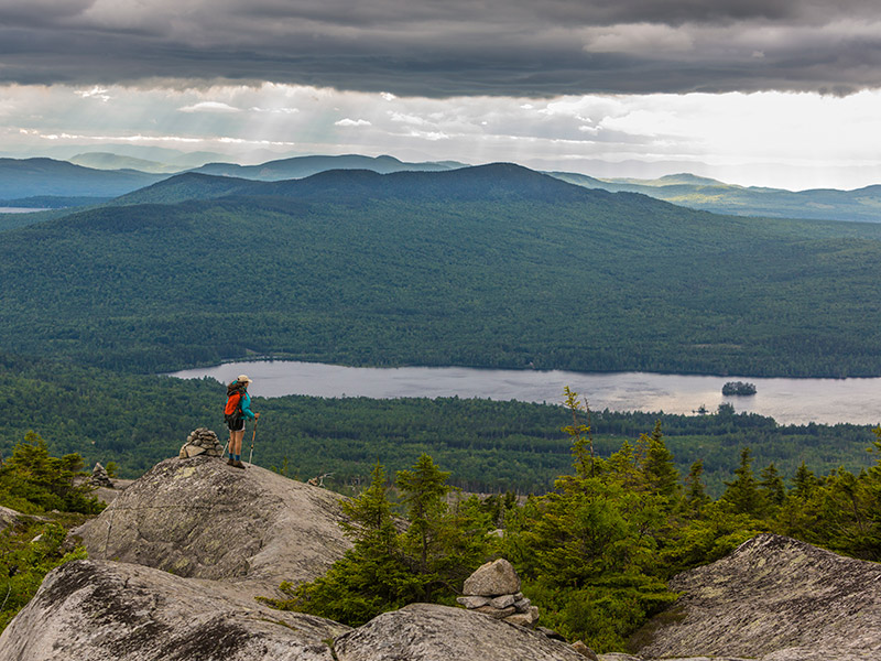 man on top of a mountain looking out at the trees lakes and the mountains in the distance