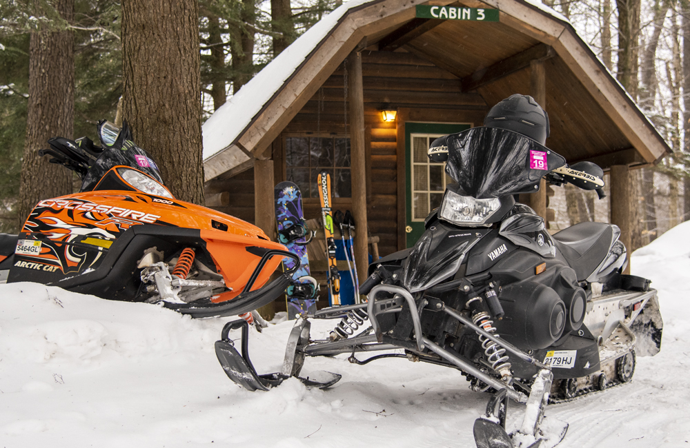 Two snowmobiles are in front of one of the cabins at Old Forge Camping Resort.