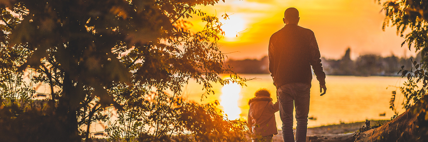 An adult and child walking to the lake before the sun sets.