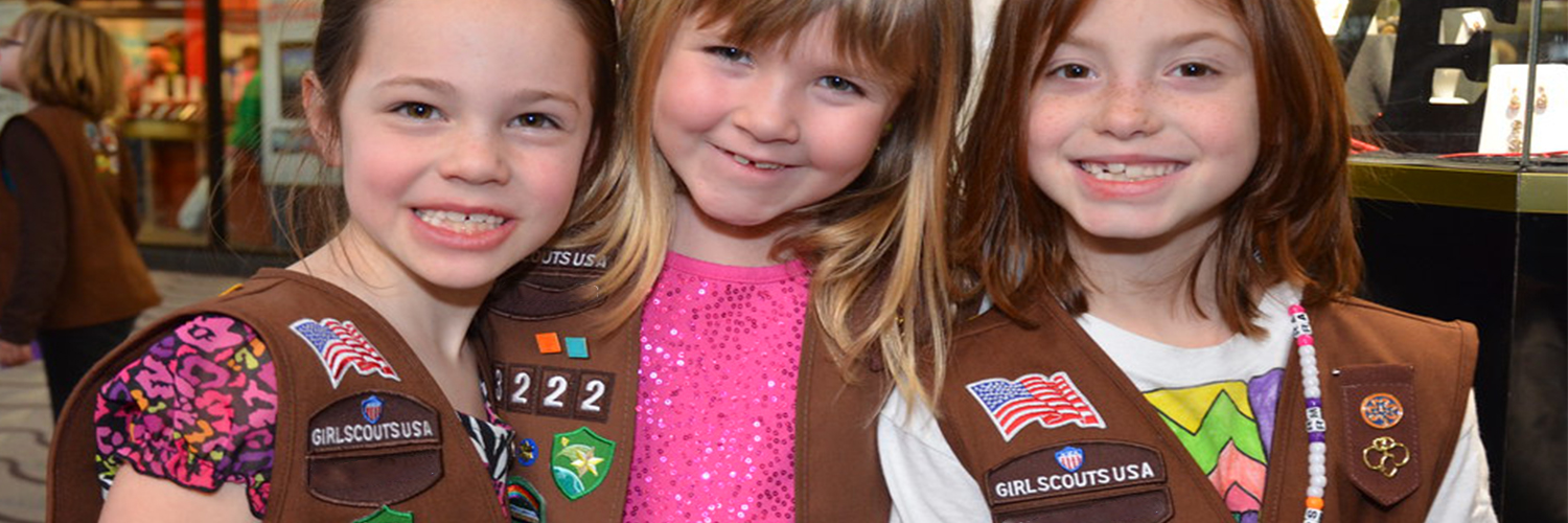 Three young girls smiling while wearing their Girl Scouts uniforms.