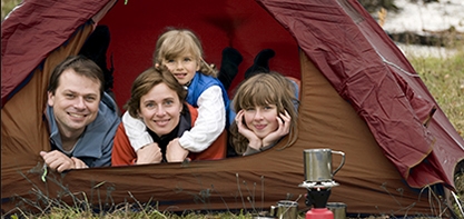 A family laying inside a tent with the flap open smiling at the camera with the lake in the background