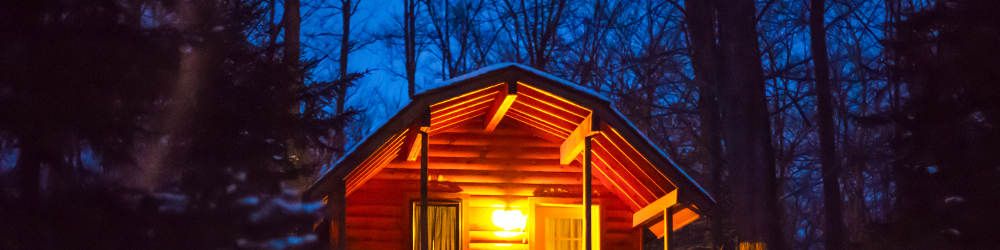 A wooden cabin at night time with the porch light on