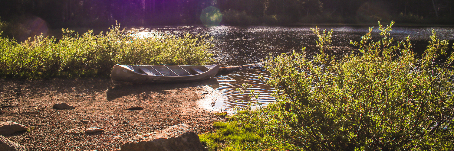 A canoe on the side of the lake. The water is calm and the sun is shining.