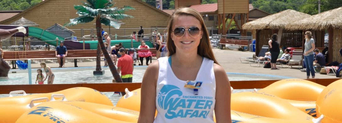 A water safari employee smiling at the camera with yellow floats behind her, cabanas to the side and a kitty pool