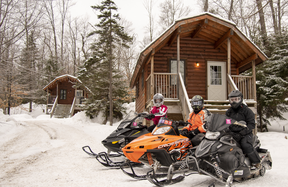 Three guests on their snowmobiles in front of their rental cabin.