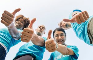 Group of adults wearing the the same volunteer shirt and giving the camera a thumbs up